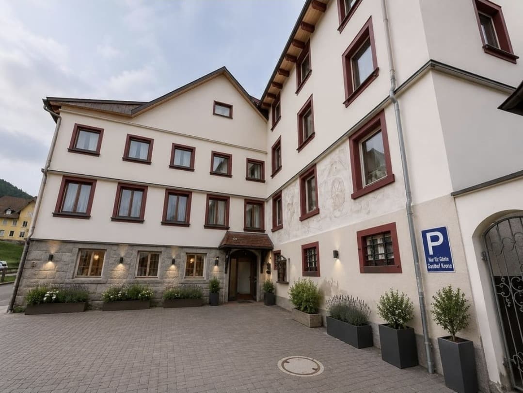 Ansicht von Hof und Eingang des Hauses nach der Renovierung: helle Fassade mit dunkelroten Fensterrahmen, gepflasterter Vorplatz mit Pflanzkübeln